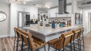 A modern kitchen with white cabinets, stainless steel appliances, and a central island with bar stools. - The Big Group Paradise: Pool, Games, & More! (North Las Vegas)