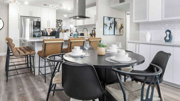 A modern kitchen with white cabinets, stainless steel appliances, and a dining area with black chairs and a round table. - The Big Group Paradise: Pool, Games, & More! (North Las Vegas)