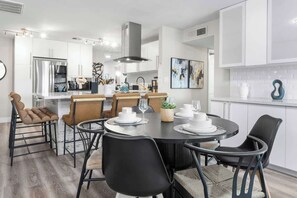 Une cuisine moderne avec des meubles blancs, des appareils en acier inoxydable et un coin repas comprenant des chaises noires et une table ronde.