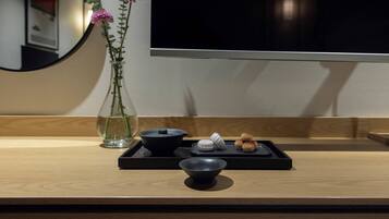 A wooden table with a black tray holding a bowl, a small black container, and some round pastries. A clear glass vase with pink flowers is on the table.