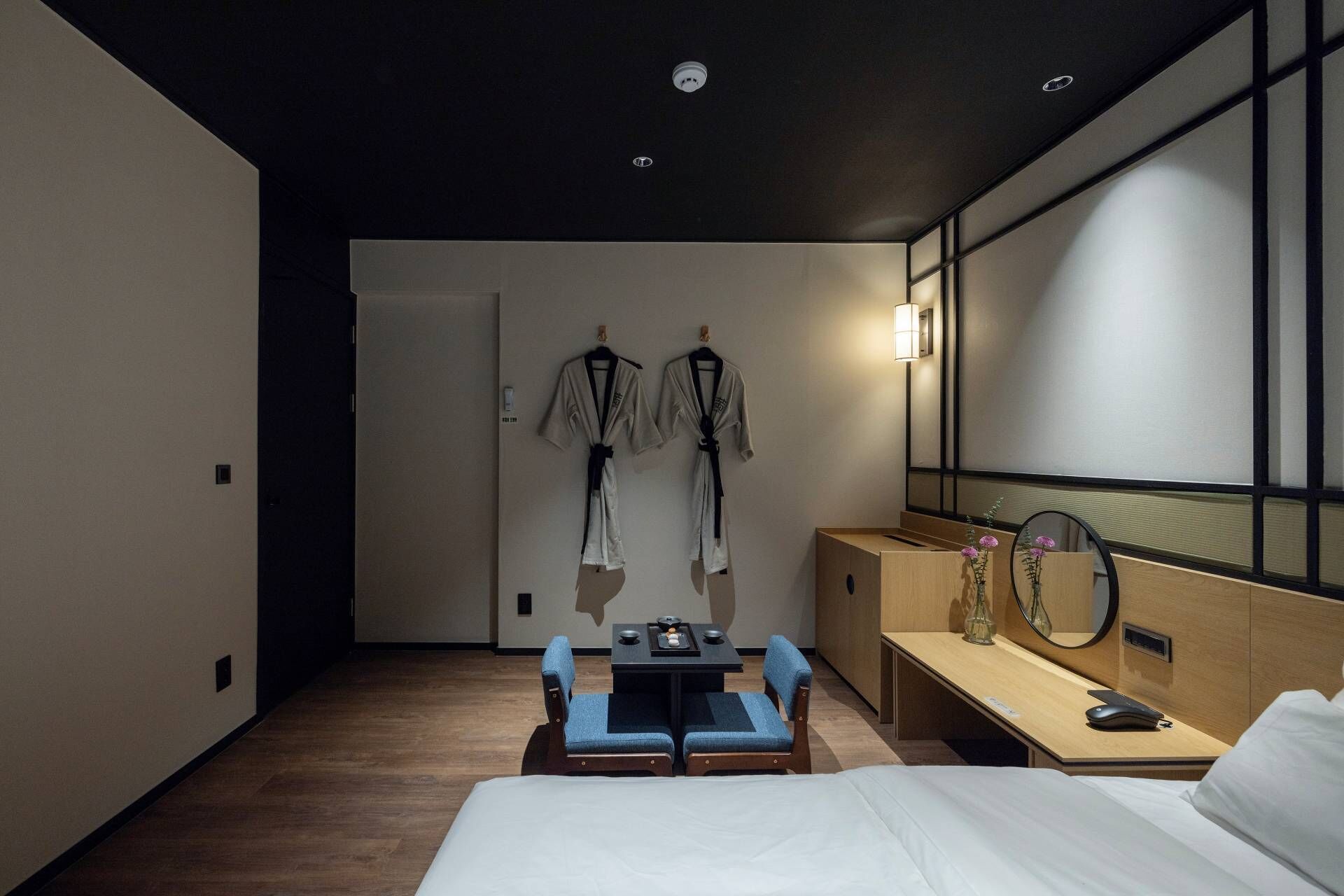 Una habitación de hotel moderna con una cama, un escritorio con espejo, una mesita con un florero y dos sillas.