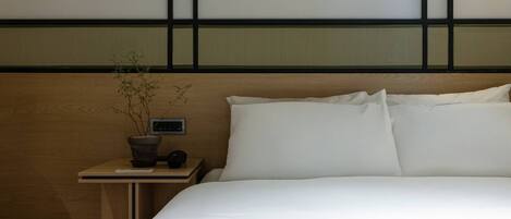 A neatly made bed with white linens in a room with a wooden headboard and a small bedside table with a potted plant.