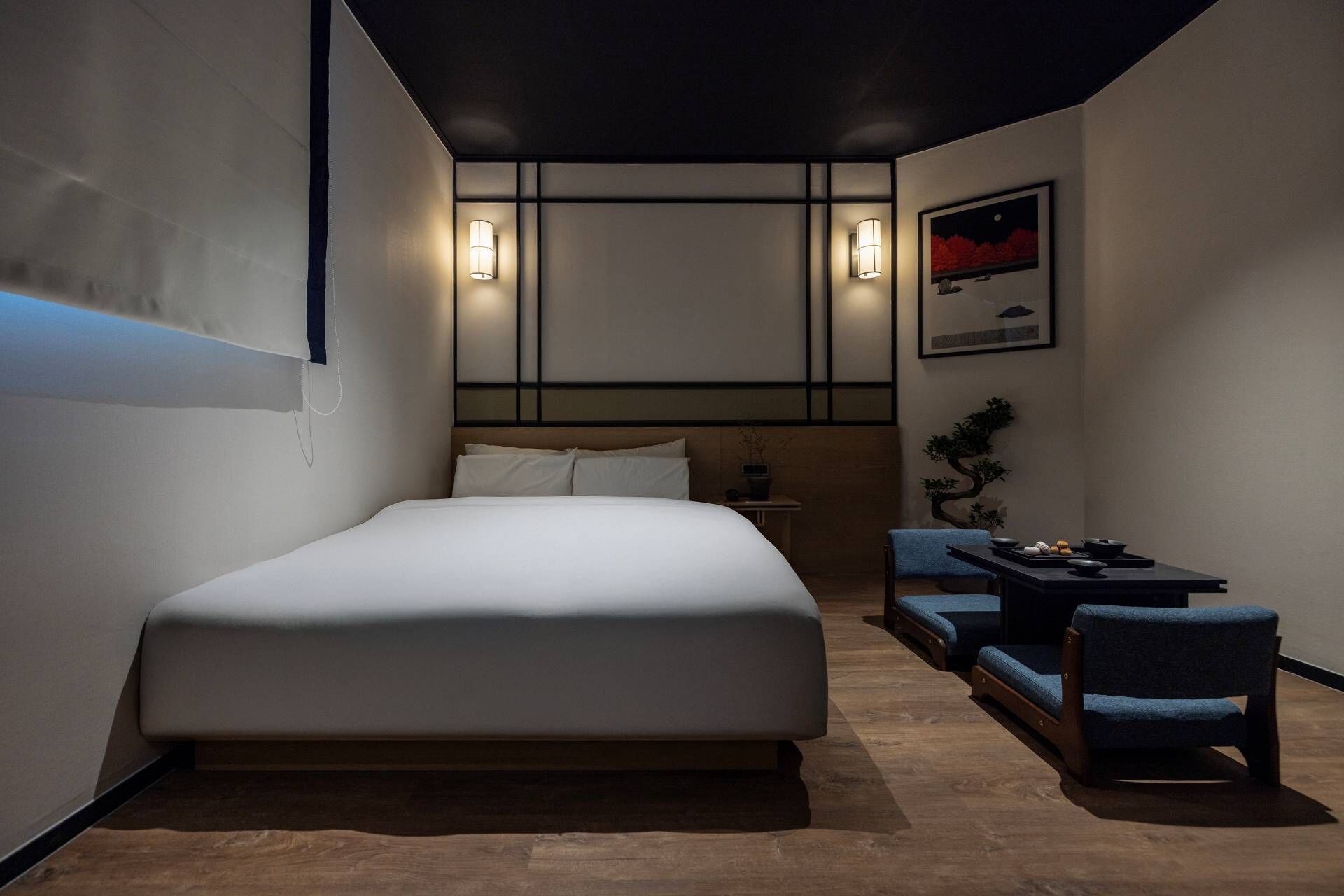 A modern hotel room with a large bed, a small seating area with a table, and a framed picture on the wall.