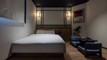 A modern hotel room with a large bed, a small seating area with a table, and a framed picture on the wall.