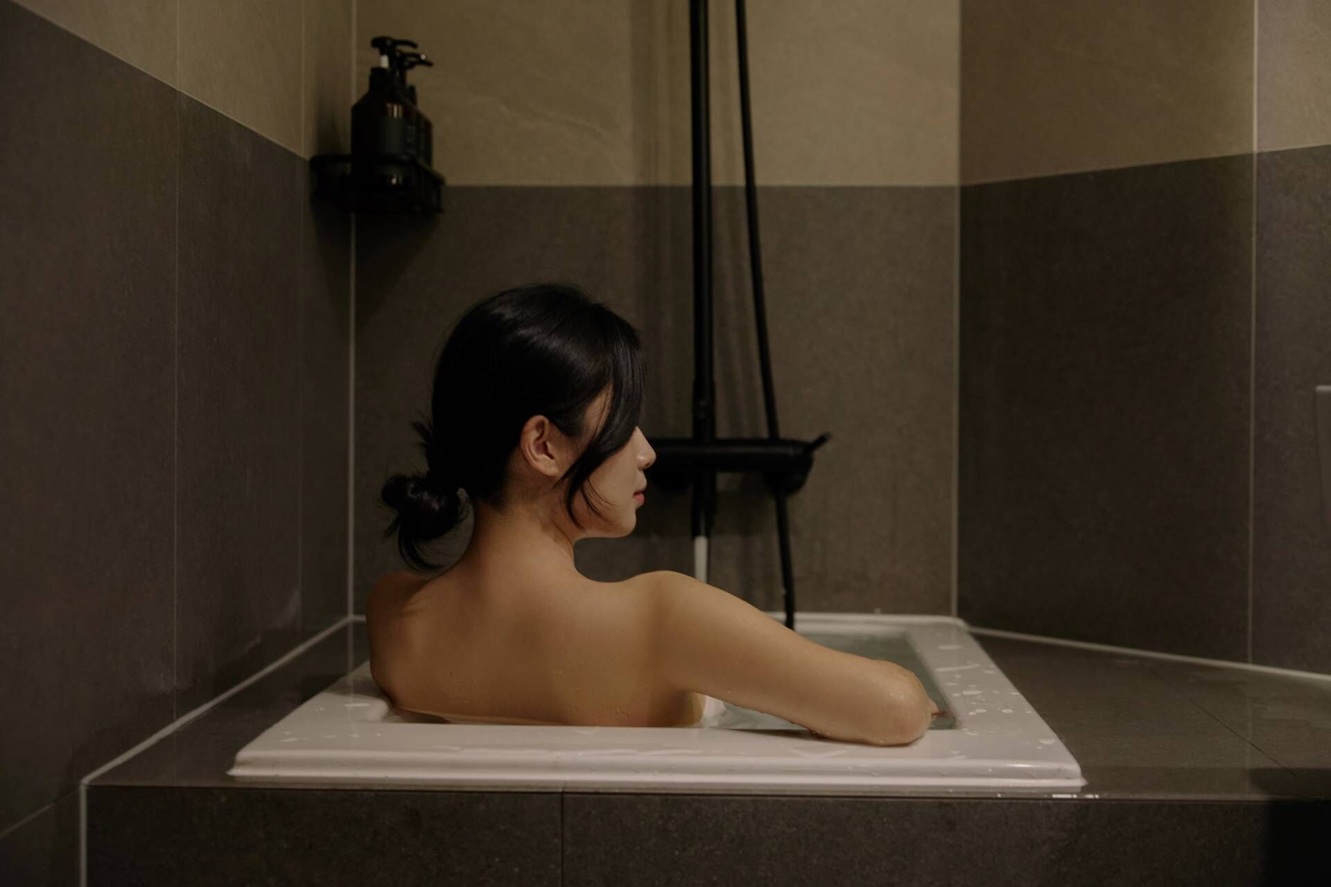 Eine Person in einer Badewanne mit einem schwarzen Seifenspender an der Wand.