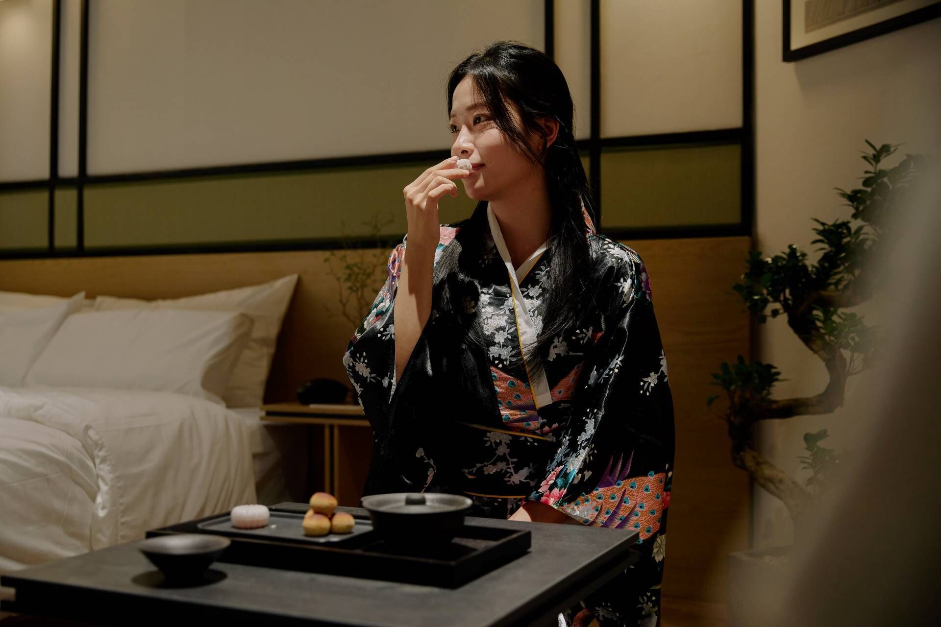 A traditional Japanese room with tatami flooring, a low wooden table with a tea set, and a bed with white bedding.