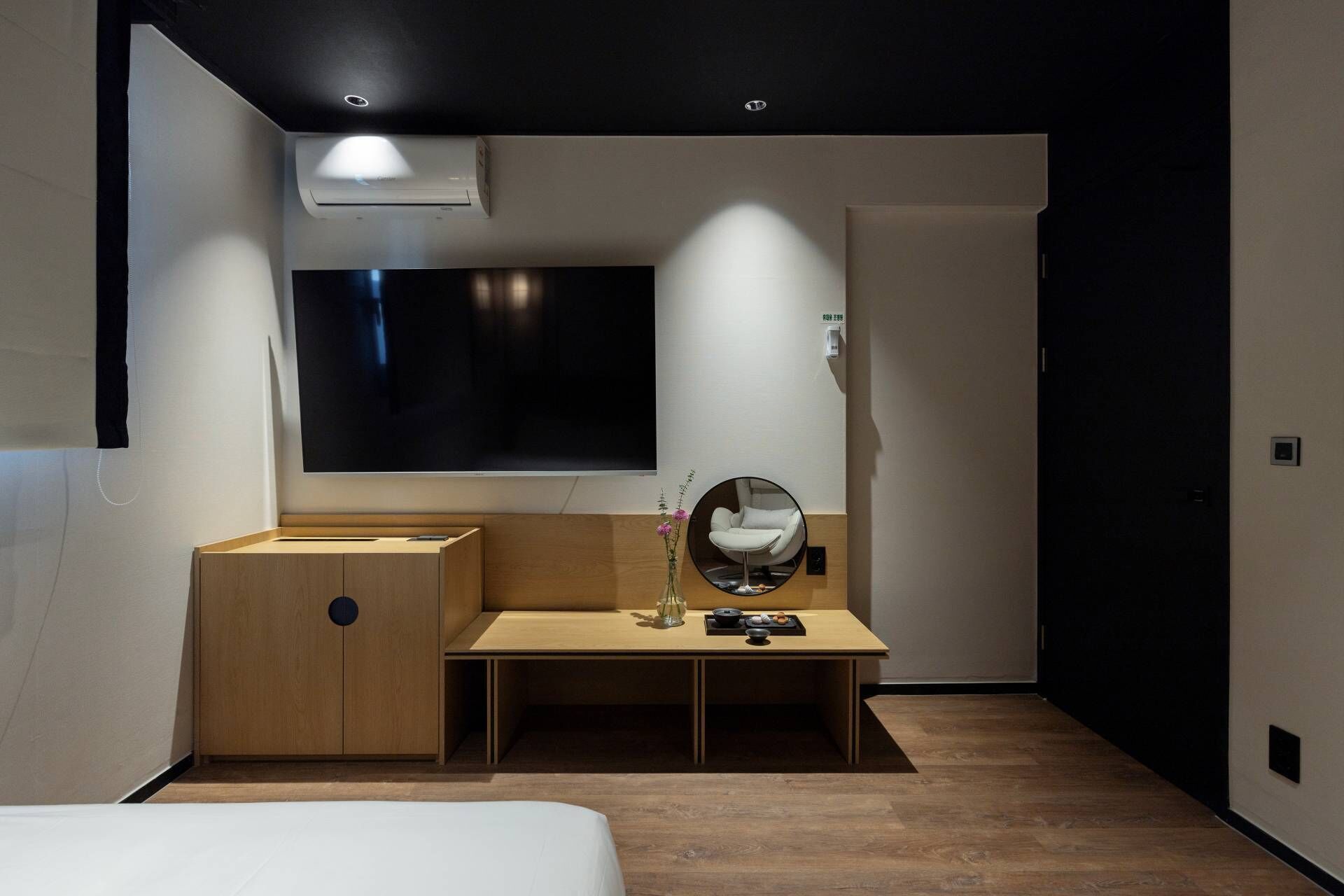 A modern bedroom with a bed, a desk, a chair, and a TV mounted on the wall.