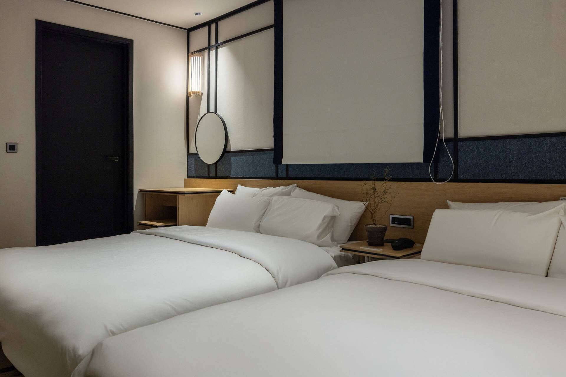 Une chambre d’hôtel avec deux lits, une table de chevet avec une lampe, un miroir et une porte.