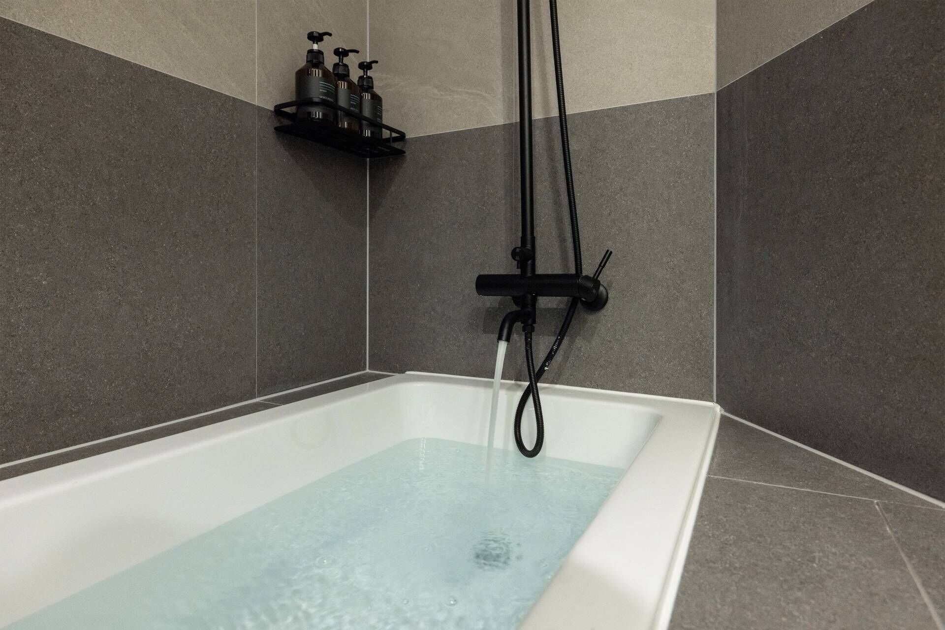 A modern bathroom with a rectangular bathtub, a showerhead, and a shelf with toiletries.