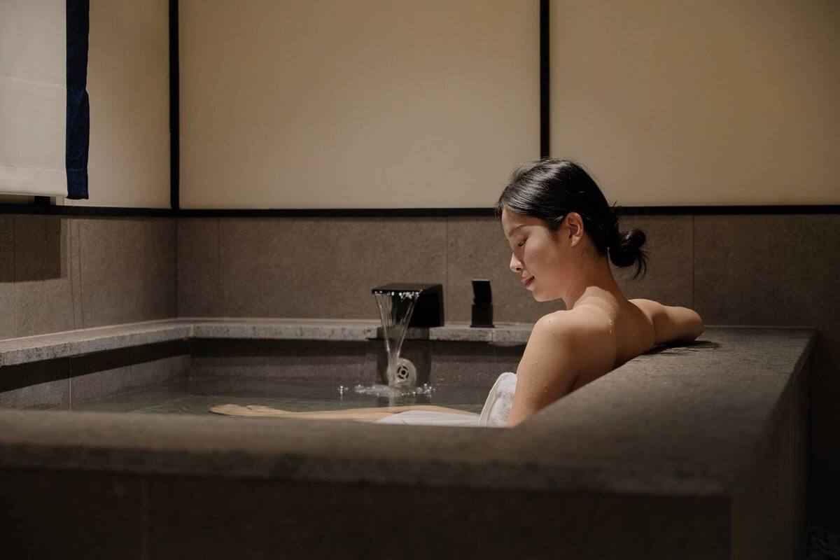 Eine Person entspannt sich in einer Steingroßbadewanne mit einer Wassersäule.