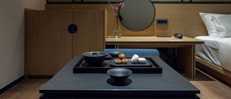Habitación de hotel con un escritorio de madera, una cama y una pequeña mesa con un bol y algunos pastelitos.