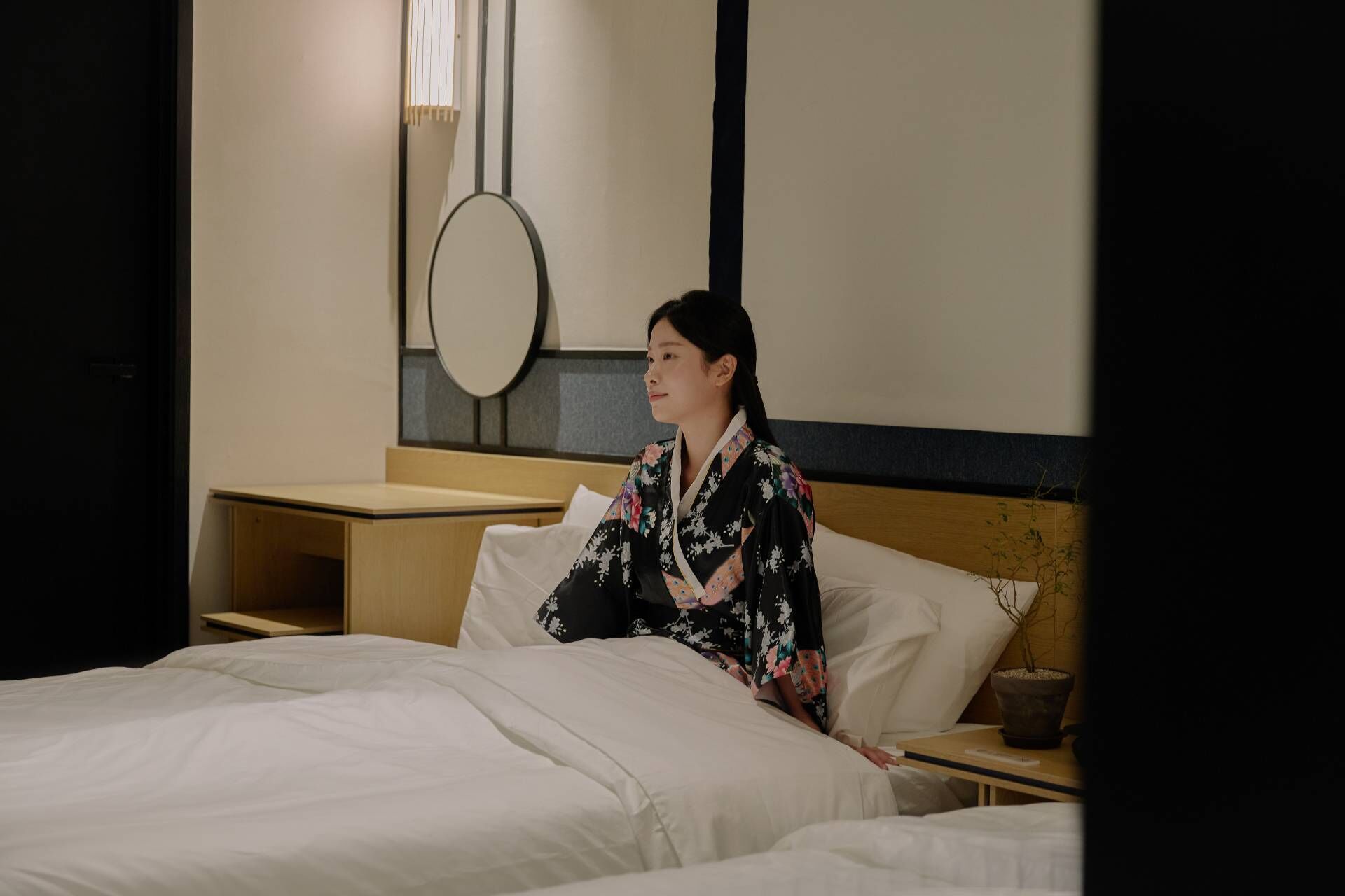 A hotel room with a bed, a nightstand, a bedside table, and a mirror on the wall.