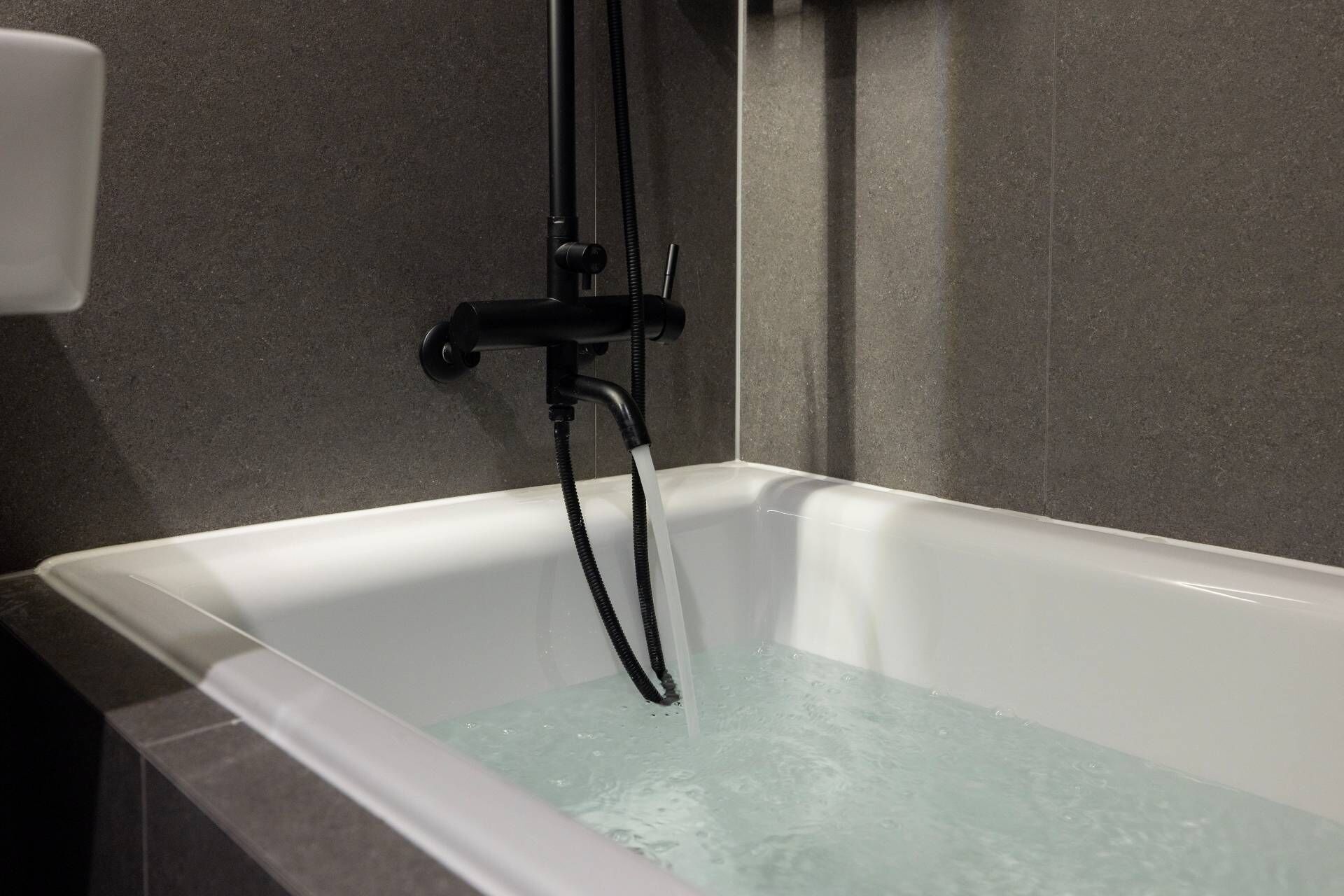 A modern bathroom with a bathtub, a handheld showerhead, and a wall-mounted faucet.