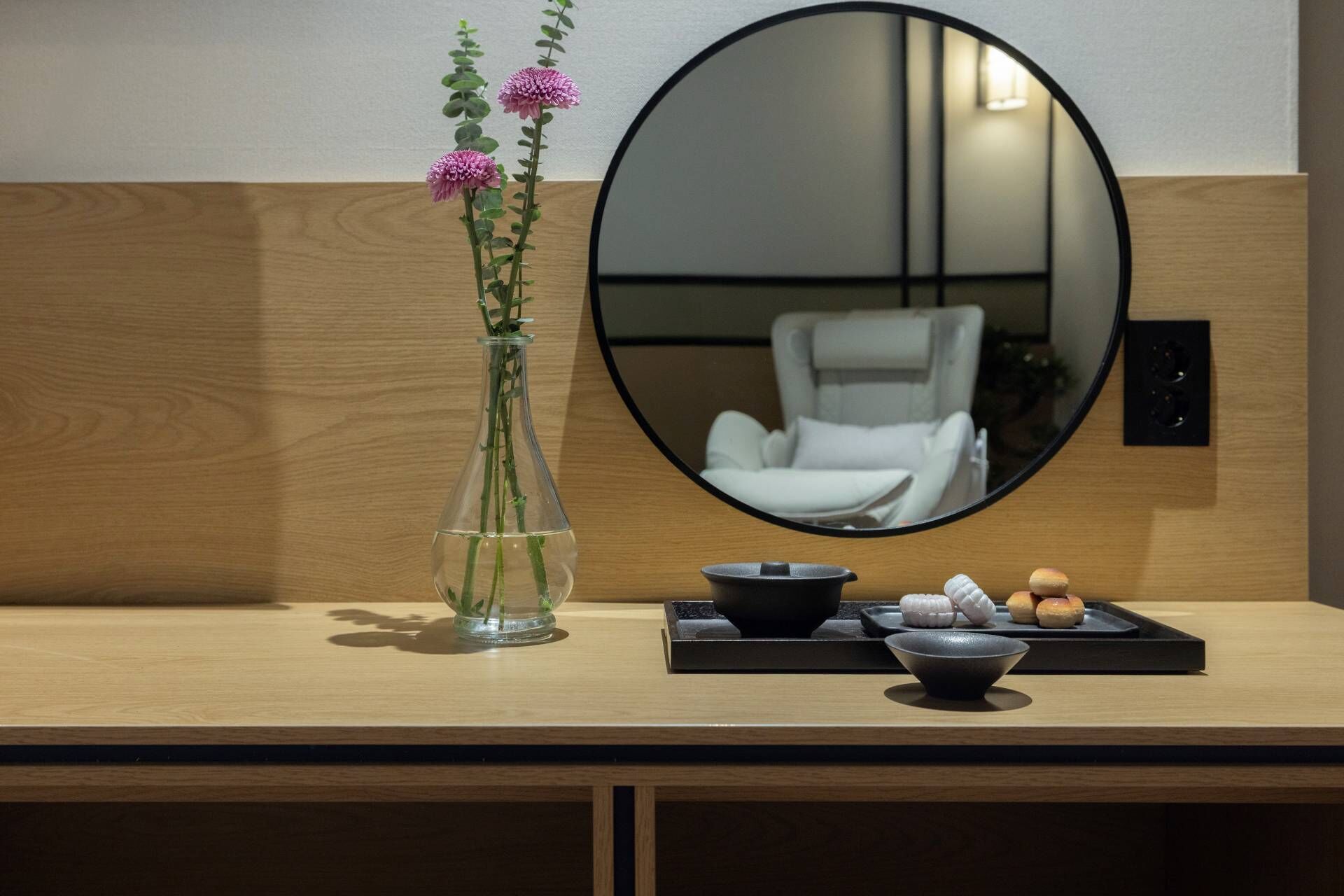A wooden desk with a vase of flowers, a mirror, and a tray with food items.