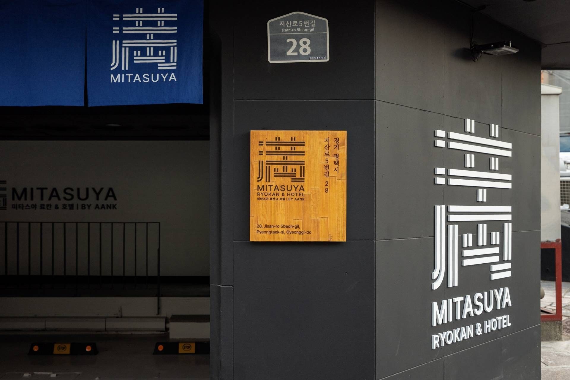 Fachada de edificio con señalización de 'Mitasuya Ryokan & Hotel' y una placa de madera con texto coreano.