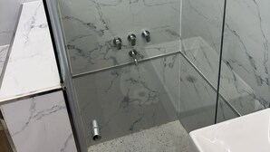 Ein Badezimmer mit Duschkabine aus Glas, Marmorwänden und einem Waschbecken.