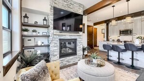 A modern living room with a stone fireplace, a round coffee table, and a seating area with a sofa and armchairs. - AC in Downtown 2/2 with Mountain Views and easy access! (Winter Park)