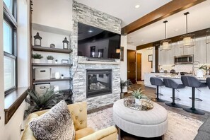 A modern living room with a stone fireplace, a round coffee table, and a seating area with a sofa and armchairs. - AC in Downtown 2/2 with Mountain Views and easy access! (Winter Park)