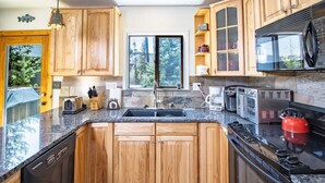 Una cucina con mobili in legno, un piano di lavoro in granito, un lavello, un fornello e un forno a microonde.