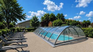 A covered swimming pool with a transparent roof, surrounded by a gravel area and benches. - The Crested Grebe. In the countryside between Lake Der, the lakes, and the forests of the East (Joncreuil)
