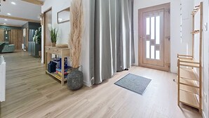 A modern interior with a wooden floor, a grey curtain, a mirror, a door with a window, and a small shelf with books and a vase. - The Crested Grebe. In the countryside between Lake Der, the lakes, and the forests of the East (Joncreuil)