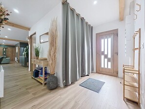 Ein modernes Interieur mit Holzboden, einem grauen Vorhang, einem Spiegel, einer Tür mit Fenster und einer kleinen Ablage mit Büchern und einer Vase.