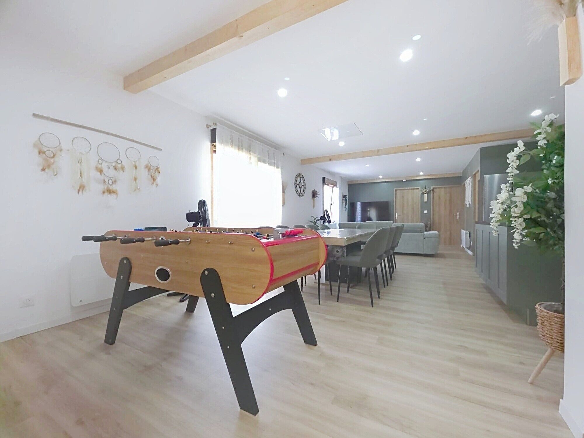 A spacious living area with a foosball table, a dining table, and a kitchen in the background.