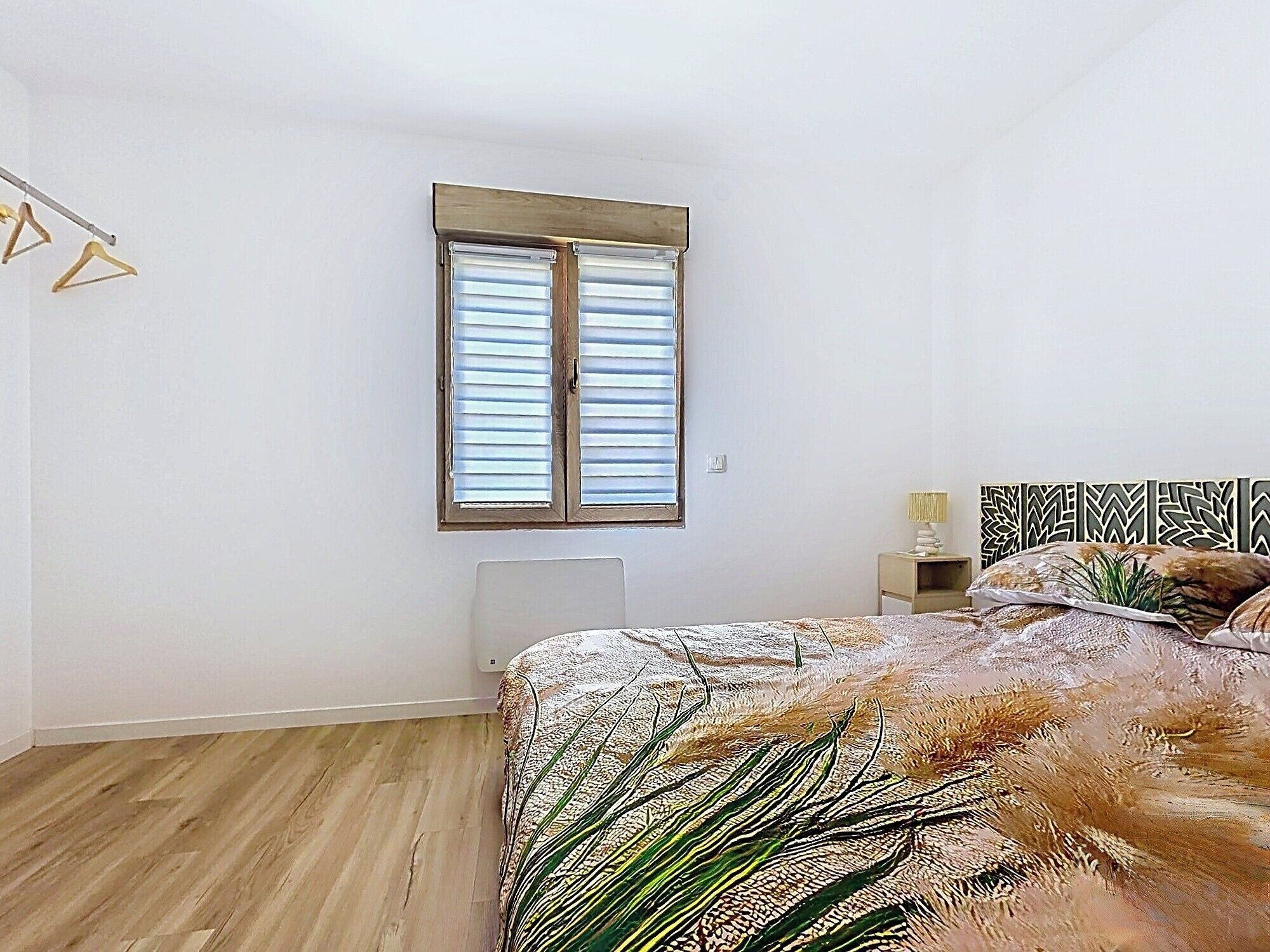 A bedroom with a bed, a window with blinds, a bedside table, and a nightstand.