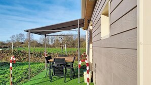 Un espace extérieur abrité, avec une table et des chaises, situé à côté d’un bâtiment dont les murs sont recouverts de bardage.