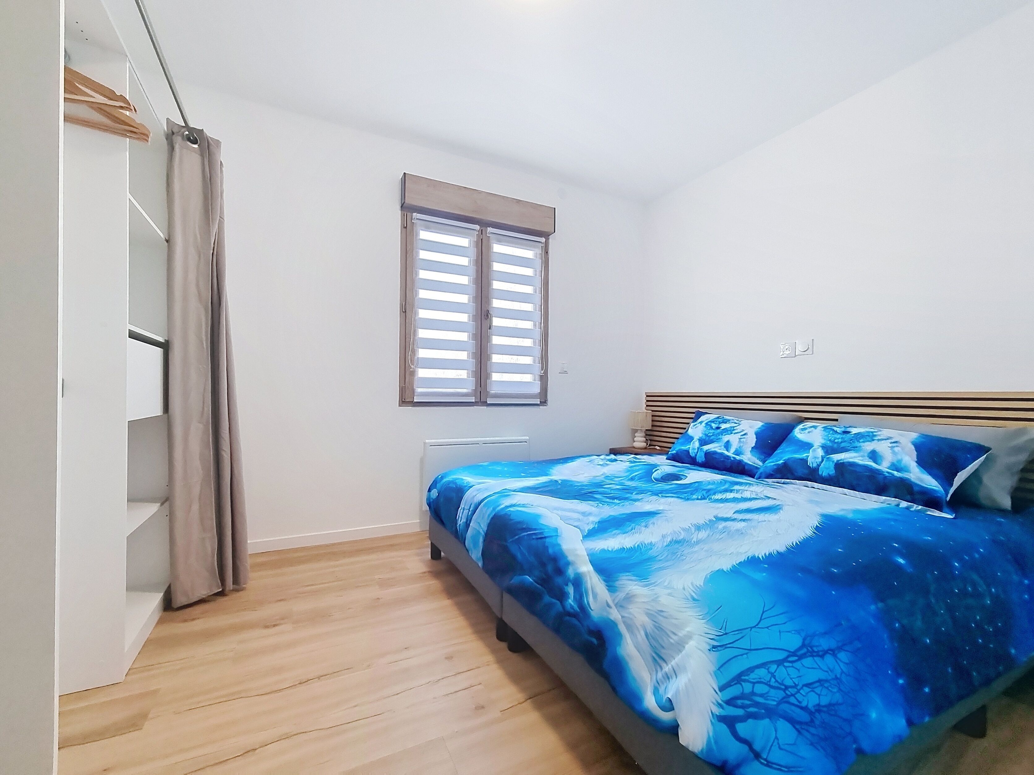 A bedroom with a bed, a window with blinds, a wardrobe, and a radiator.