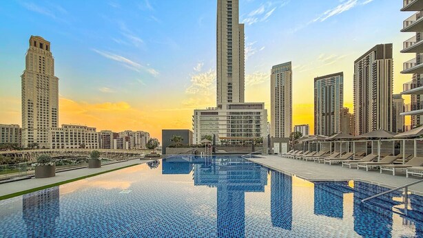 Una piscina con bordo piastrellato, circondata da palazzi e un cielo al tramonto.