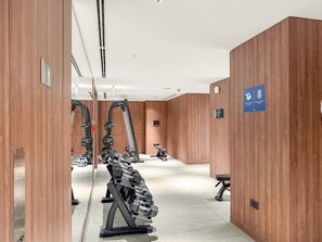 A modern gym with wooden walls, weightlifting equipment, and a clean, spacious layout. - FIRST CLASS | 2BR | The Crest • Near Attractions (Meydan)