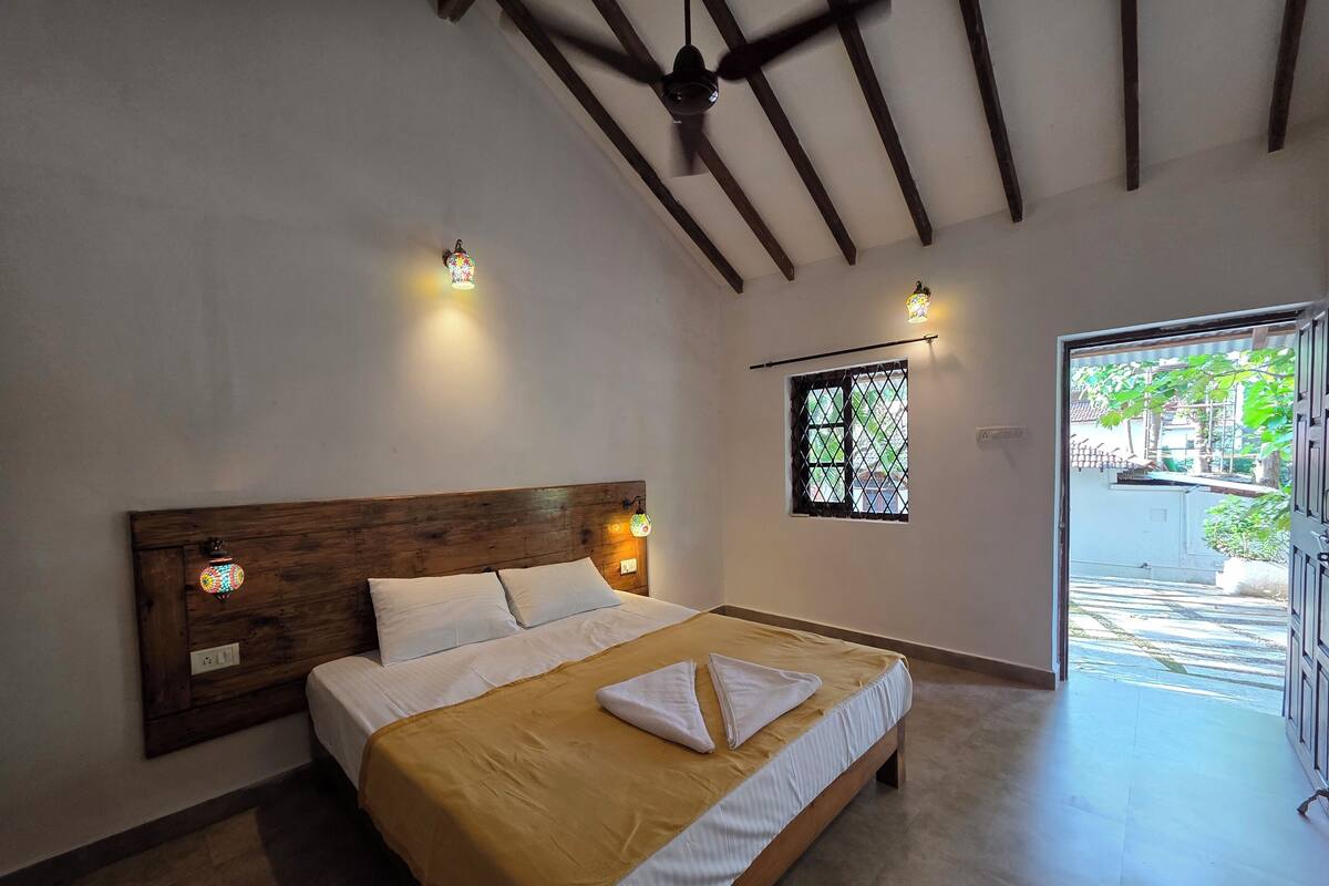 Une chambre à coucher avec une tête de lit en bois, deux lampes de chevet, une fenêtre donnant sur un beau paysage et un lit recouvert d’une couverture jaune et agrémenté d’oreillers blancs.