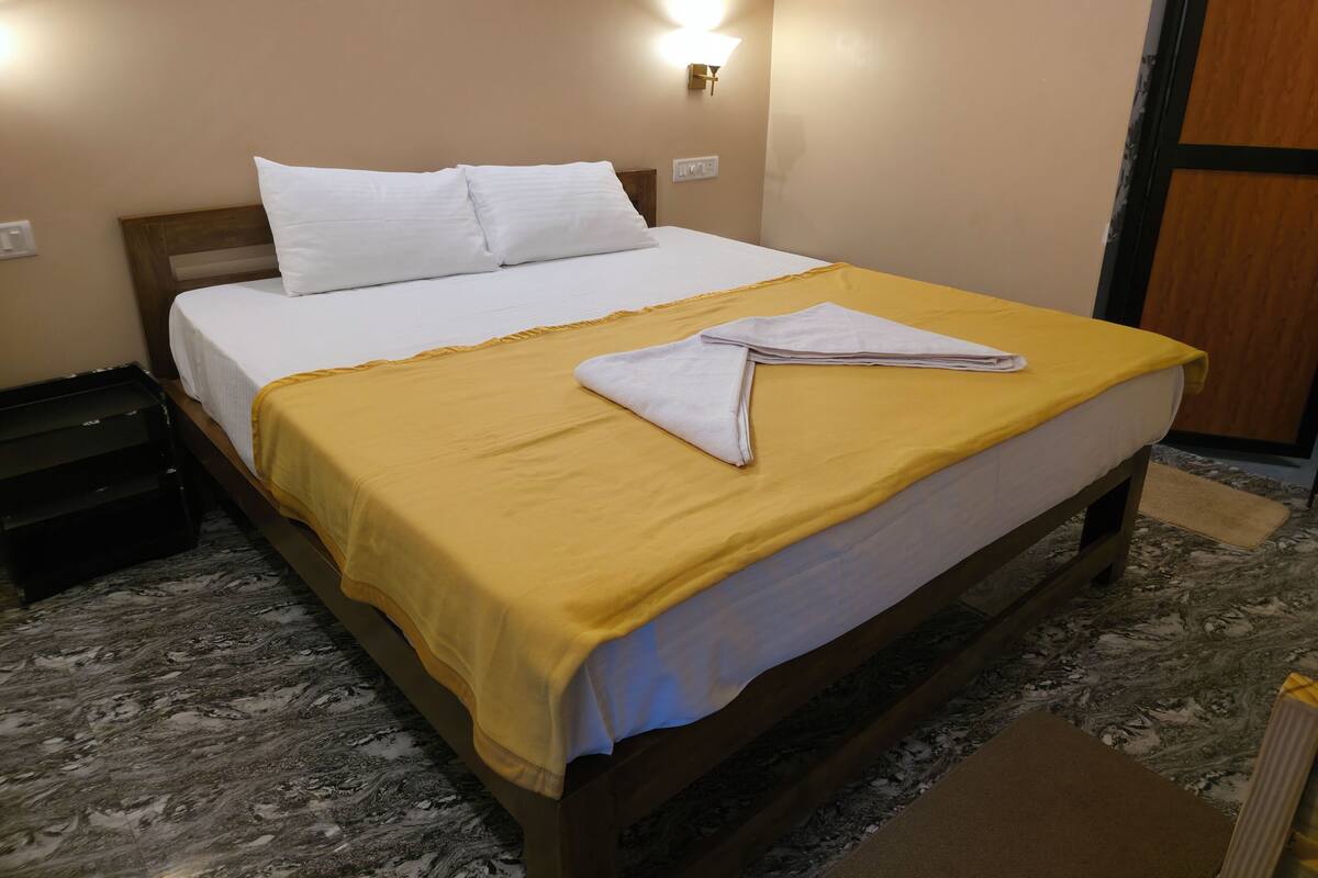 Un lit bien fait, avec une couvre-lit jaune et des oreillers blancs, une tête de lit en bois et un luminaire fixé au mur.