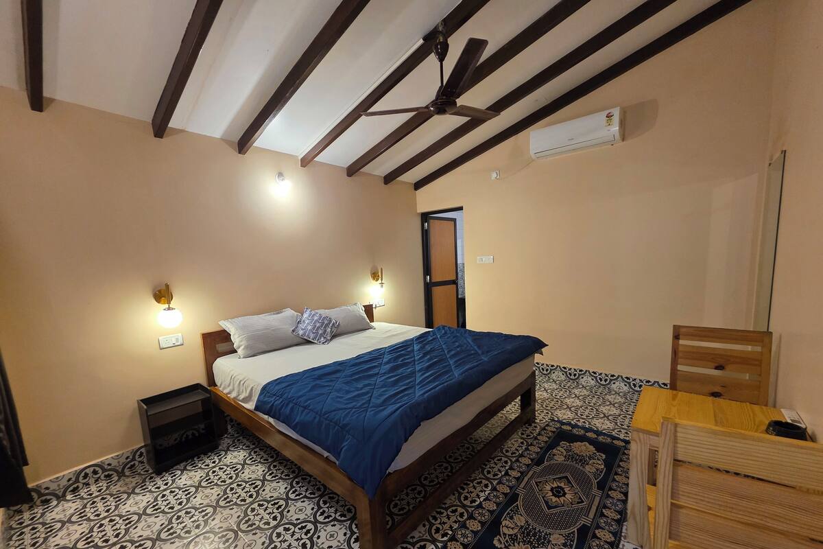 Une chambre à coucher comprenant un lit, des tables de chevet, un ventilateur de plafond, un appareil de climatisation et des carreaux de sol à motifs.