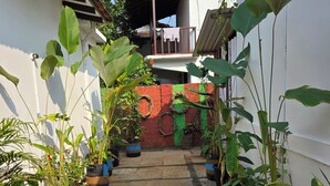 A courtyard with potted plants, a checkered floor, and a white building with a red wall. - JOE BANANA STAYS (Anjuna)