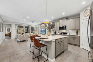 A modern kitchen with a central island, bar stools, pendant lighting, and a dining area with a sofa and coffee table. - *Recently decorated* *Game Room**Private Pool*BBQ* (Kissimmee)