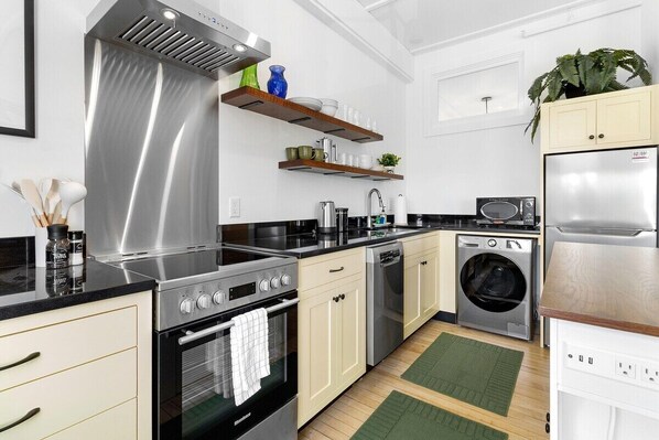 A modern kitchen with stainless steel appliances, wooden shelves, and a built-in washing machine. - Kimball Apartment, Modern Studio on Main Street Ro (Rockland)