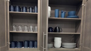 A kitchen with open cabinets containing various dishes and glassware. There is a coffee maker on the counter. - Coastal Haven-New 3BR/2BA Home, near Beaches+Fenced Yard, Pet-Friendly! (Pensacola)