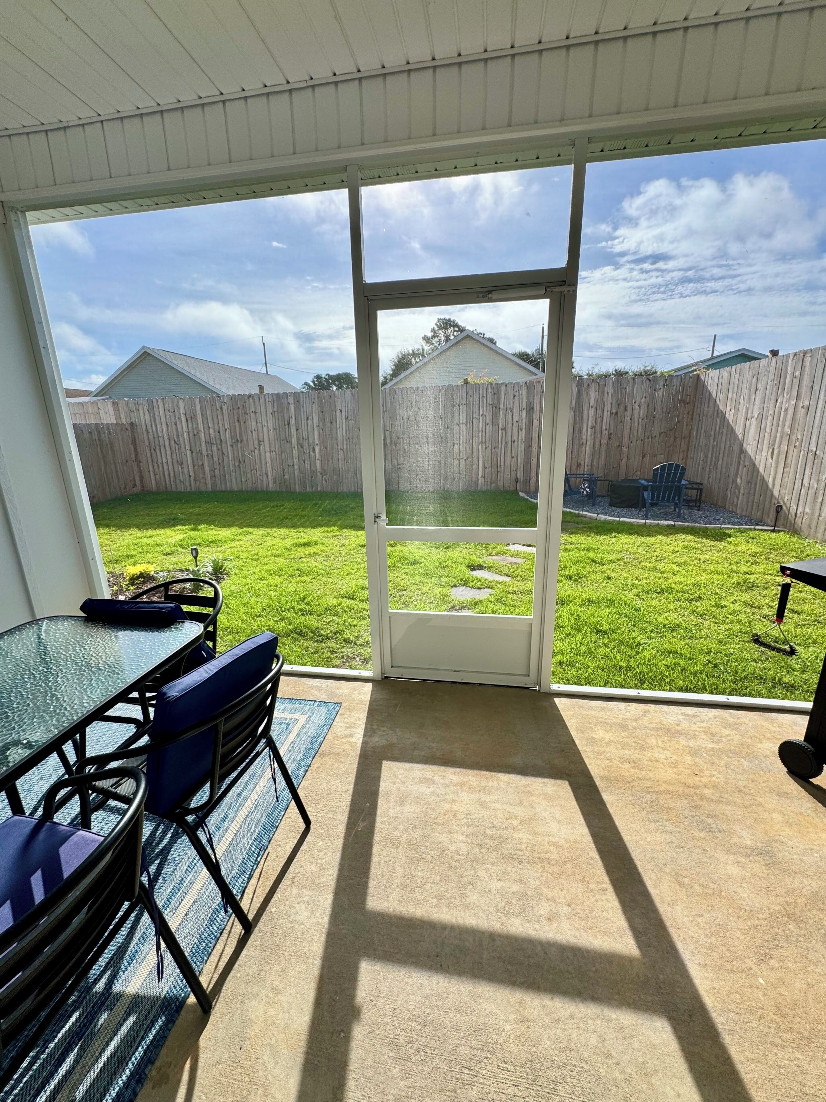A patio with a glass door leading to a backyard, a table with chairs, and a wooden fence in the background.