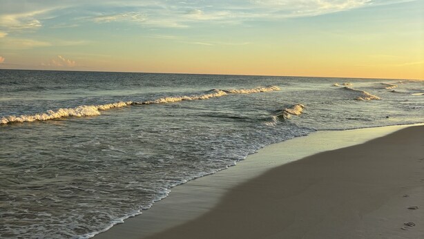 A beach with waves gently lapping onto the shore, under a partly cloudy sky. - Coastal Haven-New 3BR/2BA Home, near Beaches+Fenced Yard, Pet-Friendly! (Pensacola)