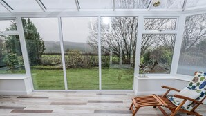 Une véranda avec un plancher en bois, une chaise en bois et une vue sur un jardin.