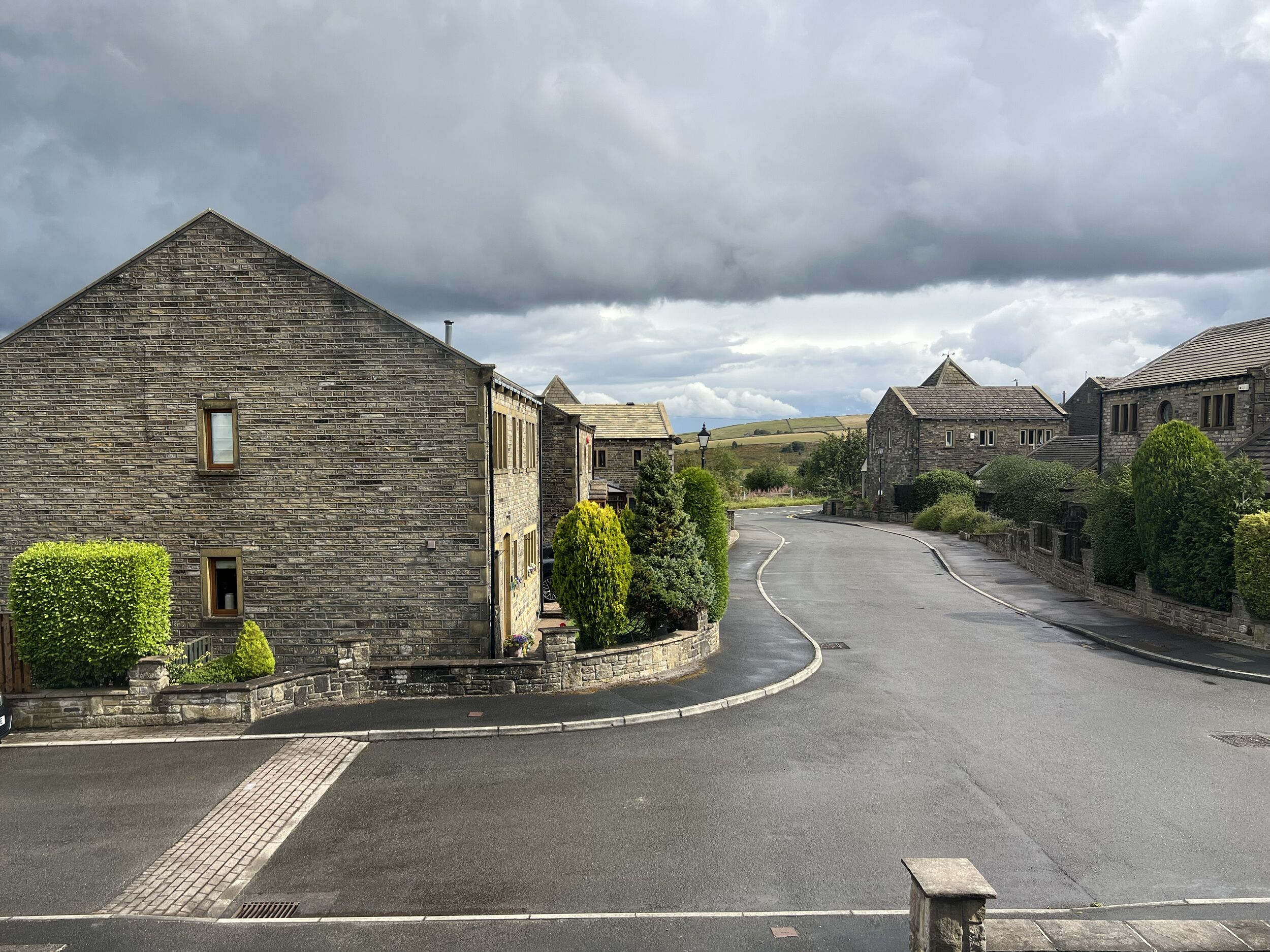 A stone building with a triangular roof, a paved road, and a curved driveway.