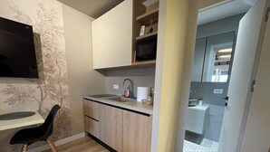 A compact kitchen with a built-in microwave, a sink, and a small countertop. There is a chair and a TV mounted on the wall. - Piazza Delux Downtown Cozy Studio (Tirana)