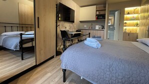 A modern hotel room with a large bed, a desk, a chair, a flat-screen TV, a microwave, and a small kitchenette. - Piazza Delux Downtown Cozy Studio (Tirana)