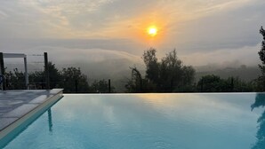 En swimmingpool med udsigt til solnedgang og omkringliggende træer.