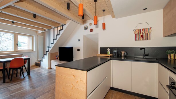 Een moderne keuken met een houten eiland, zwarte aanrechtbladen en een eetgedeelte met rode stoelen.