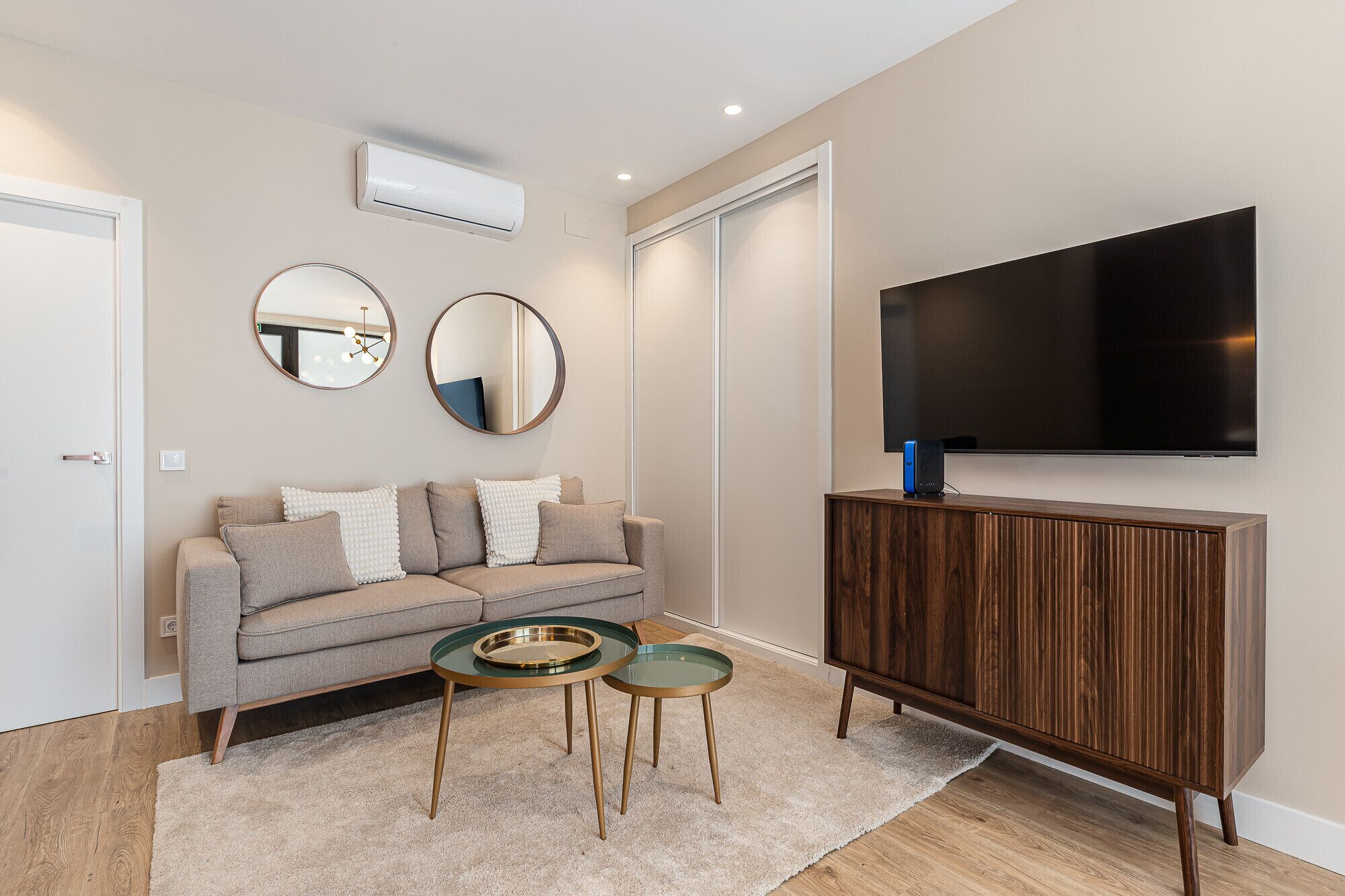 Een moderne woonkamer met een bank, twee bijzettafels, een televisie en een houten kast.