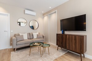 A modern living room with a sofa, two side tables, a TV, and a wooden cabinet. - Waou Essence I Bernabeu - Short Term Rental (Madrid)