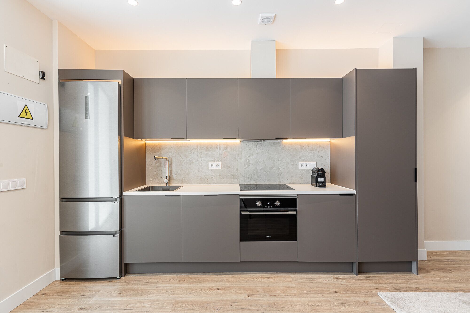 A modern kitchen with a built-in oven, a stainless steel refrigerator, and a sleek countertop.